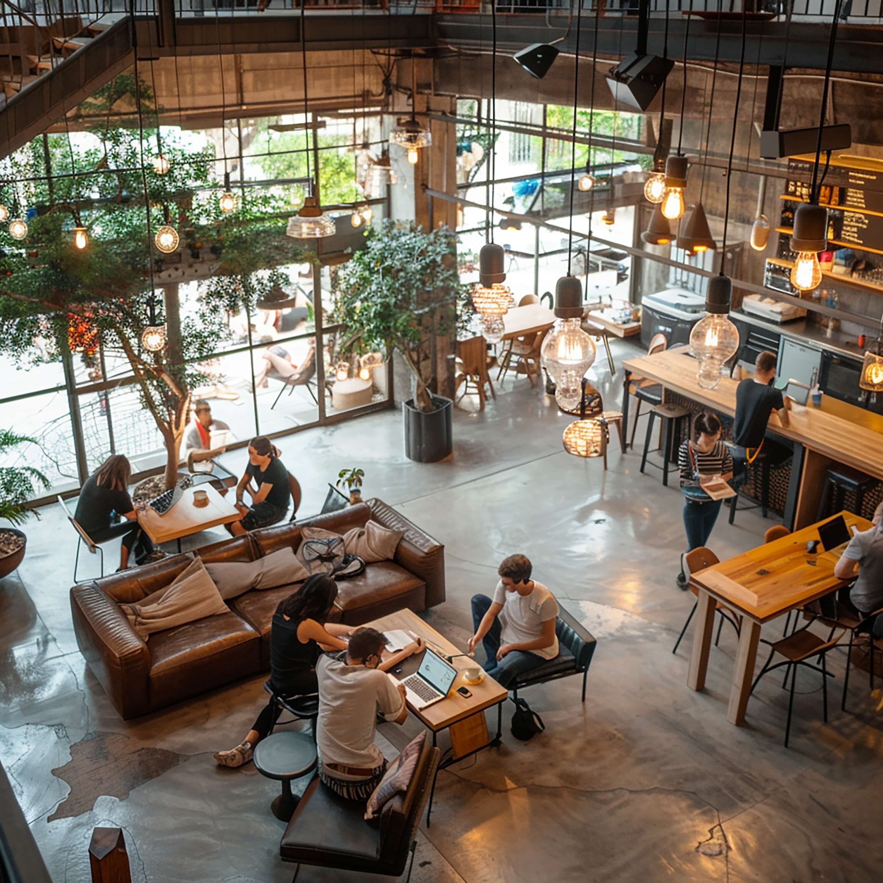 Cosy cafe interior with exposed brick, customers working on laptops. QR code displays on tables and counter.